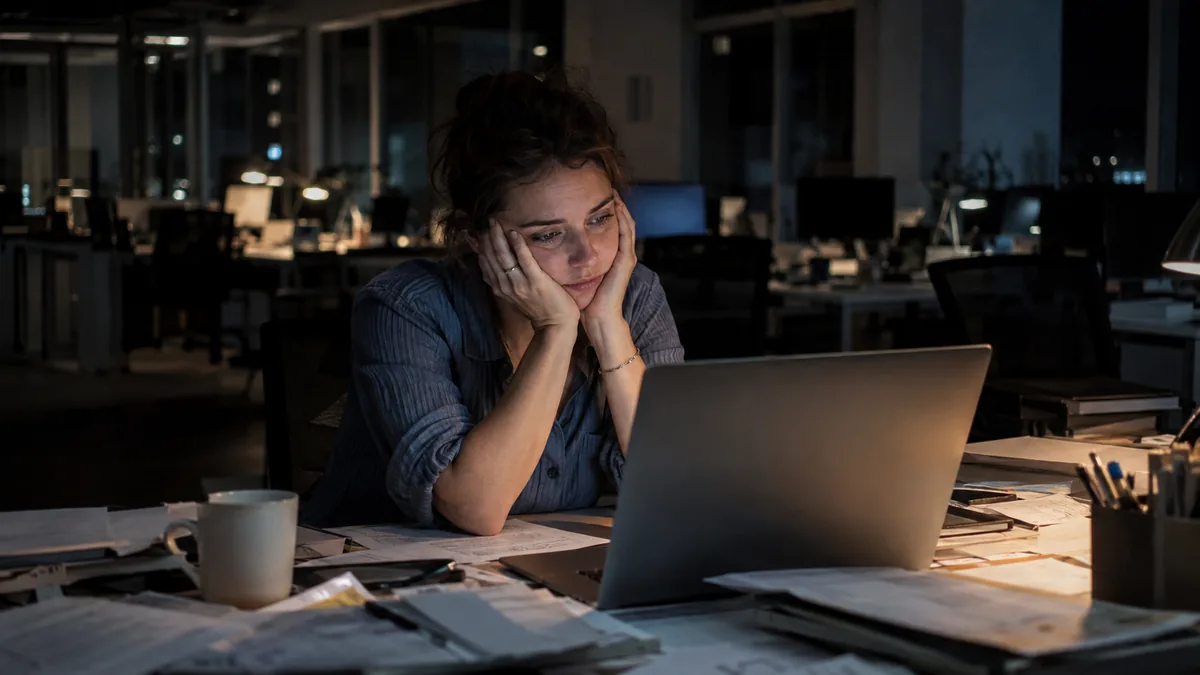 Femme épuisée, le visage dans les mains, à son bureau tard le soir